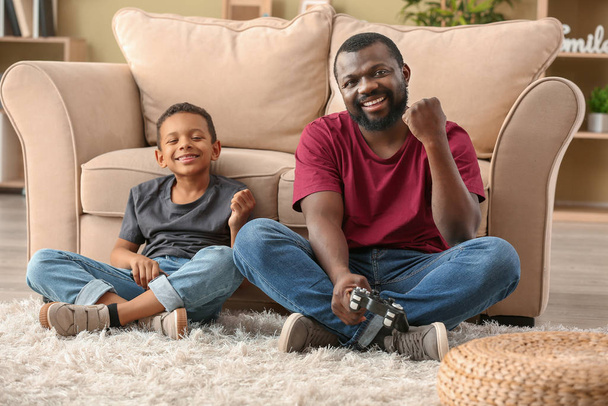 Портрет эмоционального афроамериканца и его маленького сына, играющего в видеоигры дома
 - Фото, изображение