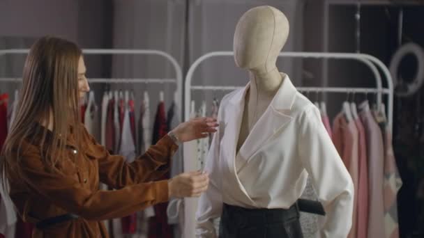 Una hermosa chica en una chaqueta mira la ropa en un maniquí, toca y considera el estilo y el tipo de tela de la ropa en el showroom
 - Metraje, vídeo