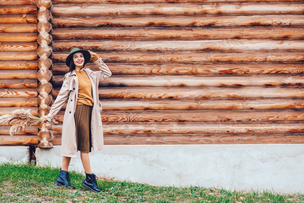 Όμορφη νεαρή γυναίκα κοντά σε ξύλινο κτίριο σε εξωτερικούς χώρους την ημέρα του φθινοπώρου - Φωτογραφία, εικόνα