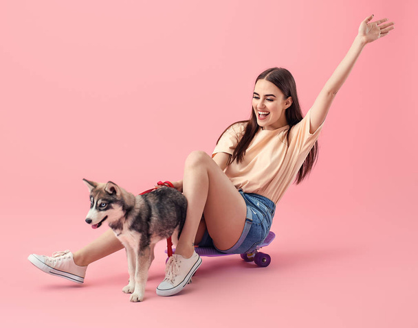 Cute woman with funny husky puppy and skateboard on color background - Photo, Image