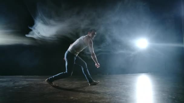 Mężczyzna tancerz wykonuje skok kaskaderski z obrotem w tył i rewolucji w scenie w dymie w świetle reflektorów. Balet współczesny. - Materiał filmowy, wideo