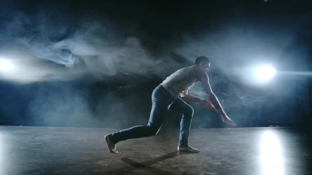 Mužský tanečník provádí kaskadérský skok s rotací zpět a revolucí ve scéně v kouři ve světle reflektorů. Moderní balet. - Záběry, video