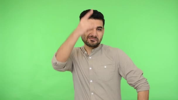 Enthusiastic crazy brunette guy in shirt showing rock and roll sign gesture, rock symbol with fingers up and making funny grimaces with tongue out. indoor studio shot, green background, chroma key - Imágenes, Vídeo
