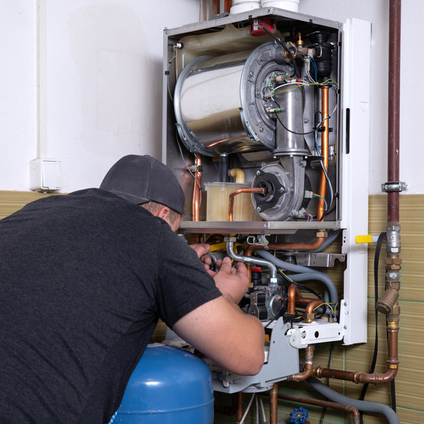сантехник фиксирует систему центрального отопления, рабочий обслуживает газовый котел
 - Фото, изображение