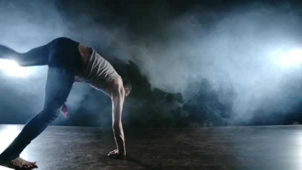 Moderní balet, muž ze sedu na jevišti skáče vzad s rotací na tmavém jevišti v kouři ve světle reflektorů - Záběry, video