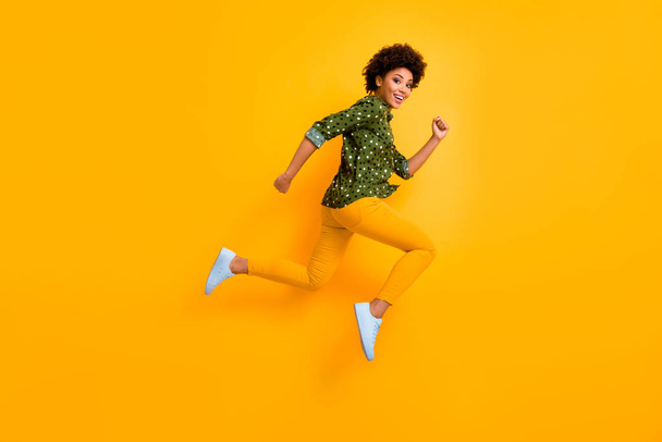 Full size photo of crazy dark skin curly lady jumping up high rushing fast discount shopping black friday low prices wear green dotted shirt pants shoes isolated yellow color background - Valokuva, kuva