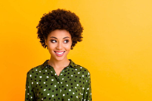 Photo of pretty funny dark skin wavy lady toothy smiling good mood easy-going person looking side empty space wear green dotted shirt blouse isolated yellow color background - Foto, afbeelding