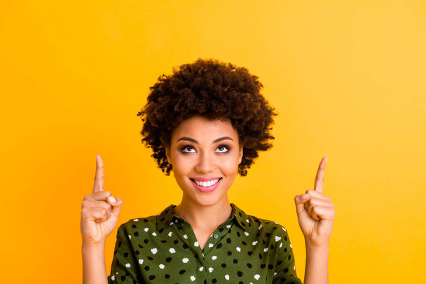 Close up photo of positive cheerful afro american girl promoter point index finger copy space indicate look adverts promotion wear stylish clothes isolated yellow color background - Fotoğraf, Görsel