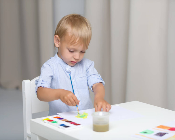 Cute little boy paints with watercolors while sitting at the tab - Φωτογραφία, εικόνα