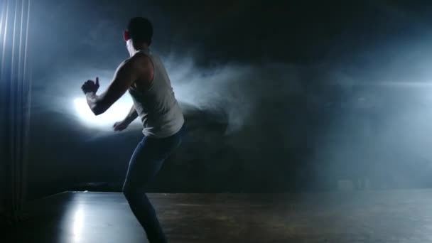 Современный балет, человек совершает прыжки и вращается в свете прожекторов и дыма на темном фоне. Акробатическая хореография, репетиция сценария современного балета
 - Кадры, видео