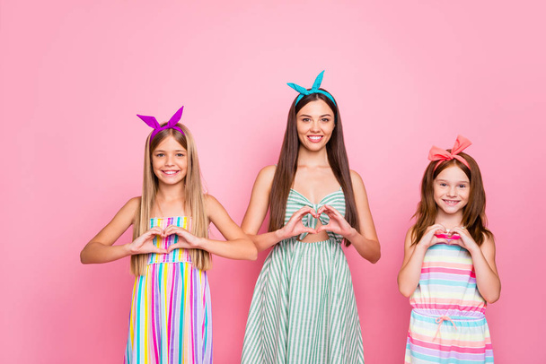 Portrait of cheerful ladies kid making heart shaped signs with their fingers wearing headbands skirt dress isolated over pink background - Foto, afbeelding