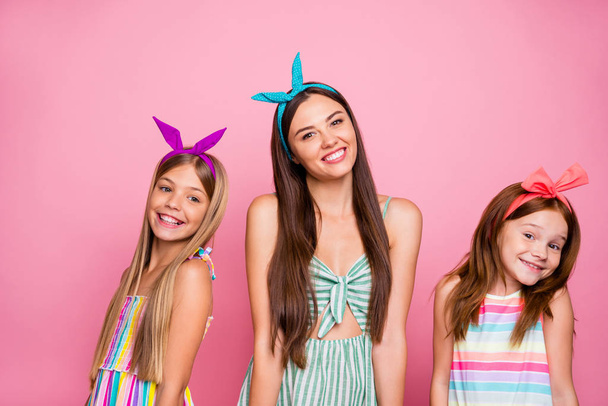 Portrait of charming three girls posing with beaming lovely smile wearing bright headbands skirt dress isolated over pink background - Фото, зображення