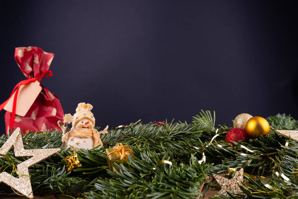 Enfeites de Natal (homem de neve, presente, estrelas, bugigangas) e galhos de abeto na frente de um fundo preto
 - Foto, Imagem