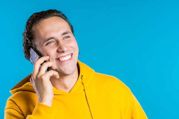 Young man in bright colorful yellow wear talking on mobile cell phone on blue background. Trendy guy have conversation. Smartphone, technology concept. - Foto, Bild