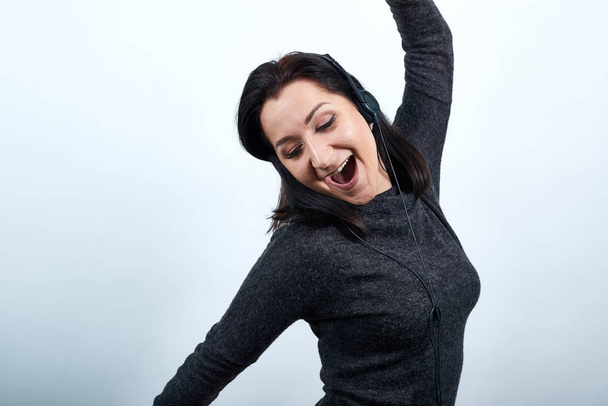Mujer joven en suéter negro se estira con los ojos cerrados, levantando las manos
 - Foto, Imagen