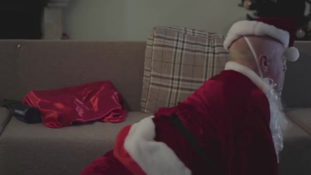 Extremely drunk Caucasian senior man in Santa Claus costume crawling to the couch. Bad Santa after the holiday. Alcoholism, depression, negativism, loneliness. - Felvétel, videó