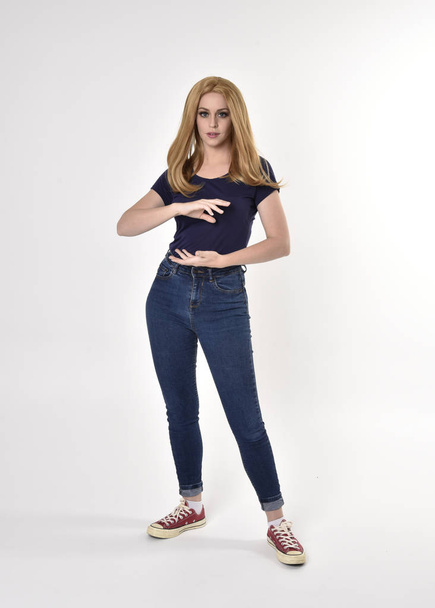 Портрет красивой блондинки в повседневной синей рубашке, джинсах и кроссовках. Стойкая поза на студийном фоне
. - Фото, изображение
