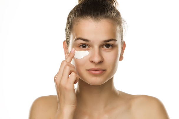 A young woman applying cream under her eyes on white background - Foto, immagini