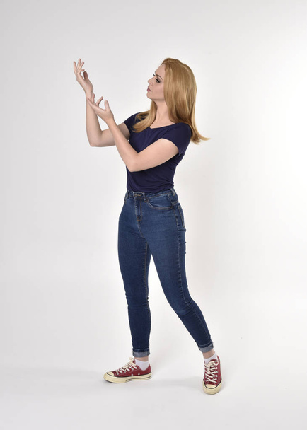 Ganzkörperporträt eines hübschen blonden Mädchens in lässigem blauem Hemd, Jeans und Turnschuhen. stehende Pose auf einem Studiohintergrund. - Foto, Bild