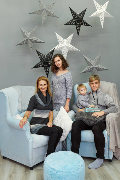family of four mother and siblings teens and toddler dressed in life style sitting on armchairs in a living room decorated with huge stars - Photo, image