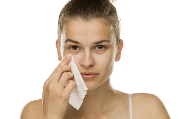 Mujer joven limpiando su cara con una toallita húmeda sobre fondo blanco
 - Foto, Imagen