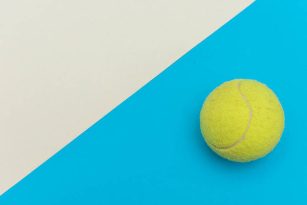 Żółta piłka tenisowa na solidnym jasnoniebiesko-białym płaskim tle leżała symbolizująca sport i aktywność z przestrzenią do kopiowania. - Zdjęcie, obraz