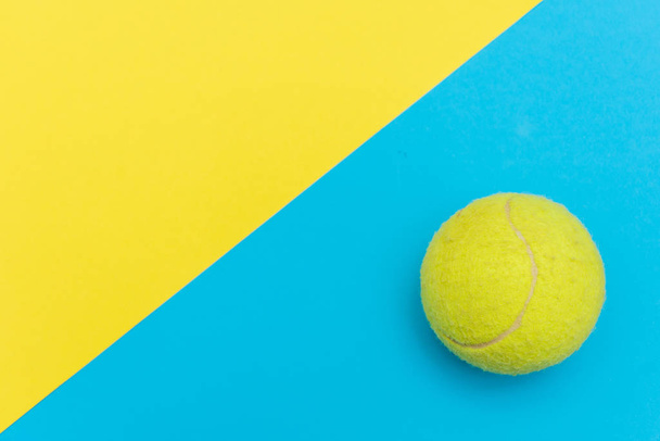 gelber Tennisball auf einem festen, hellblauen und gelben flachen Hintergrund, der Sport und Aktivität mit Kopierraum symbolisiert. - Foto, Bild