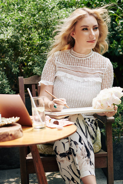 schöne elegante junge Frau, die in Skizzenbuch zeichnet, wenn sie auf einem Café im Freien ruht - Foto, Bild