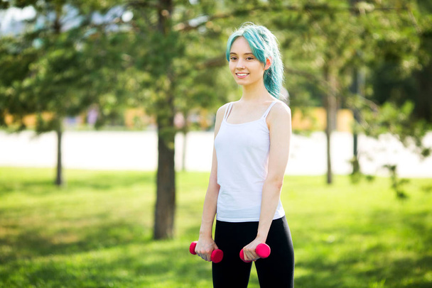 beautiful young woman goes in for sports with dumbbells in the summer in the park - Foto, Imagem