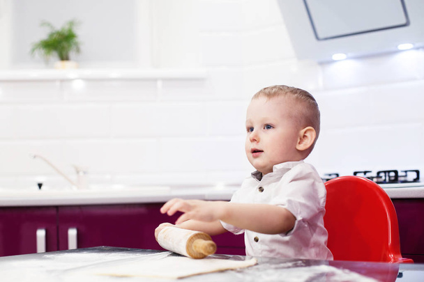 Kleiner Junge bereitet Teig zu. Junge knetet Teig in der Küche. Kind rollt Pizzateig aus. - Foto, Bild