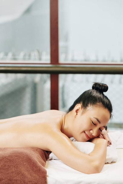 Счастливая молодая женщина отдыхает на кровати в спа-салоне после массажа спины или косметических процедур
 - Фото, изображение