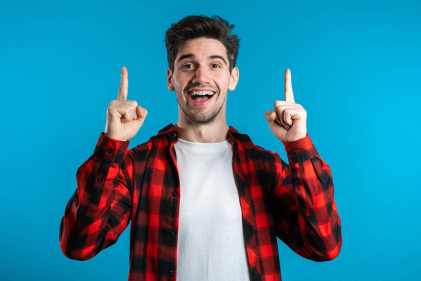 Portrait of young thinking pondering man in red having idea moment pointing finger up on blue studio background. Smiling happy student guy showing eureka gesture. - Фото, зображення