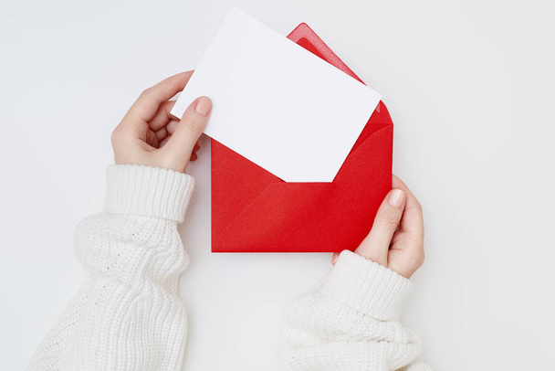 女性の手は白い背景に空のポストカードと赤い封筒を保持します。クリスマスのコンセプト - 写真・画像