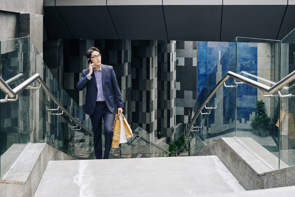 Впевнений азіатський чоловік несе паперові мішки, підіймаючись сходами від станції метро. - Фото, зображення