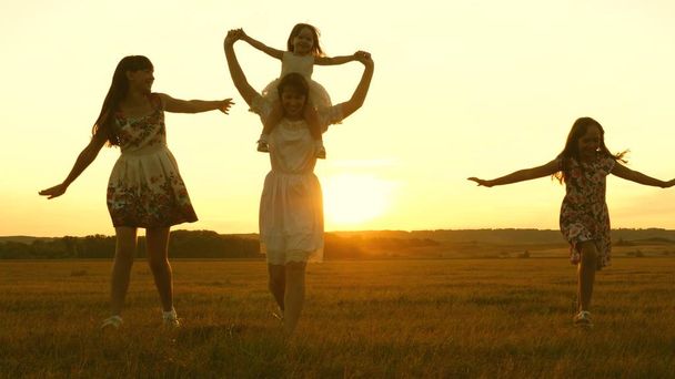 happy childhood concept. Happy young family with a child run across field in flight at sunset light. Mother and daughters walks in park and play in the meadow in sun. concept of life of a large family - Foto, immagini