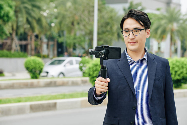 Asian man in glasses making video on smartphone attached to monopod - Fotografie, Obrázek