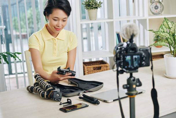 Sorridente bella giovane donna asiatica riprese video recensione di treppiedi e monopodi a casa
 - Foto, immagini