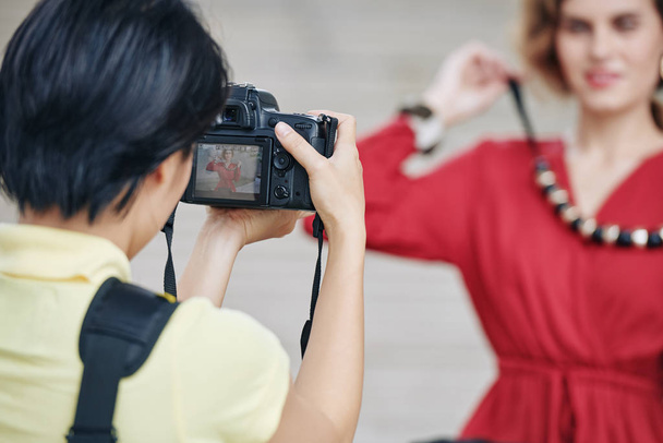 Nainen valokuvaaja käyttää digitaalikameraa kuvatessaan houkutteleva nuori nainen massiivinen kaulakoru ulkona
 - Valokuva, kuva