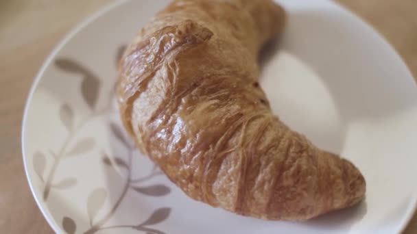 Draufsicht auf leckeres frisches Croissant, das auf dem weißen Glasteller liegt, französisches Frühstückskonzept. Archivmaterial. Nahaufnahme von schönen Teigwaren auf der Holzoberfläche. - Filmmaterial, Video