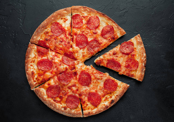 Snijd peperoni pizza op zwarte achtergrond - Foto, afbeelding
