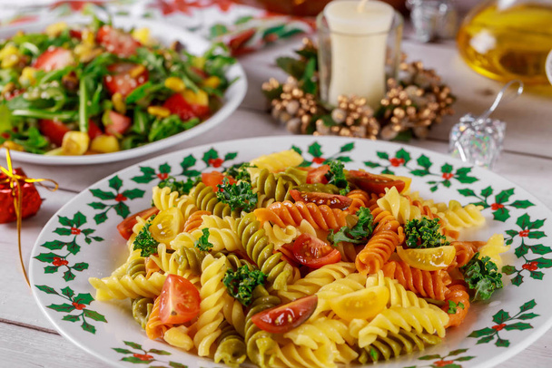 Colorful pasta rotini, cherry tomatoes on christmas table with salad. - Photo, Image