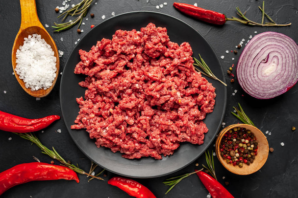Minced meat in black bowl on table with ingredients - Foto, afbeelding
