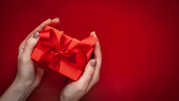 Female hands holding red gift box on background with copy space - Zdjęcie, obraz