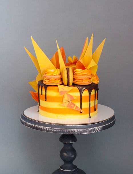 Orange and yellow coloredcake with chocolate decor, candles and macaroons on grey background.  - Fotoğraf, Görsel