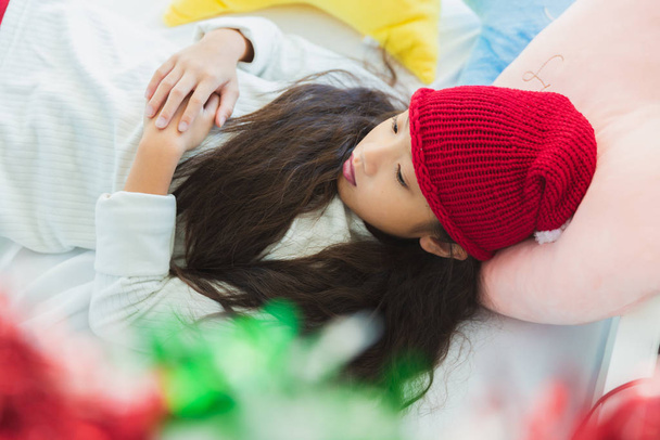 Αξιολάτρευτη Ασιάτισσα με Χριστουγεννιάτικο καπέλο που κοιμάται σε λευκό κρεβάτι - Φωτογραφία, εικόνα