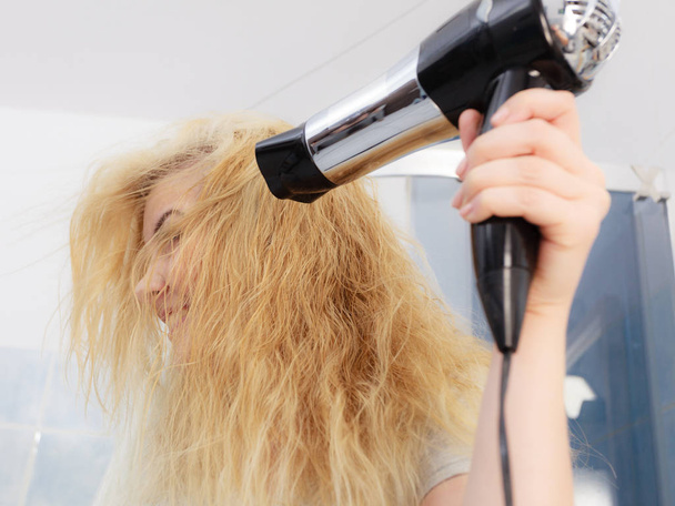 Blonde woman using hair dryer - Foto, afbeelding