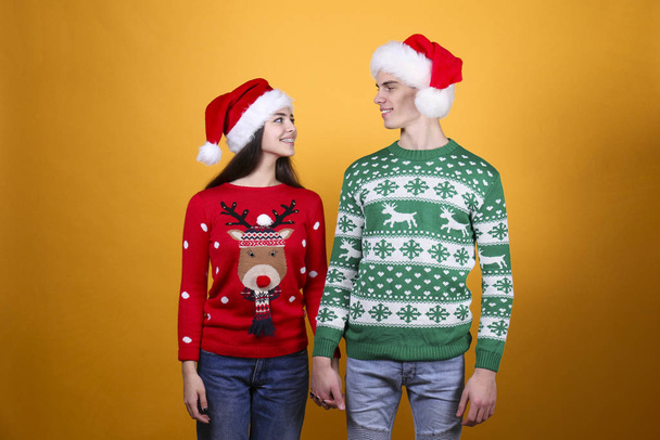 Couple of young people wearing ugly christmas sweaters, posing over colorful isolated background. - 写真・画像