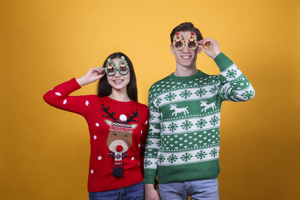 Couple of young people wearing ugly christmas sweaters, posing over colorful isolated background. - Valokuva, kuva