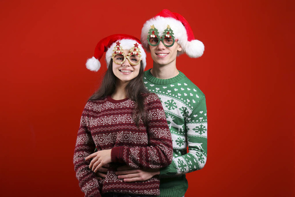 Ein paar junge Leute in hässlichen Weihnachtspullovern posieren vor buntem Hintergrund. - Foto, Bild