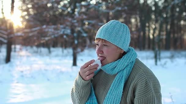 Mujer comiendo nieve en el bosque de invierno. Divertida señora mayor lamiendo hielo al aire libre como una broma con ropa de abrigo. Clima frío estacional
 - Imágenes, Vídeo